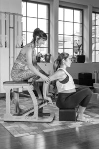 Pregnant client using the wunda chair during a Pilates class with teacher assisting