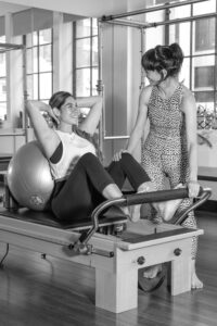 Pregnant client supported on reformer with a fitball and teacher assisting